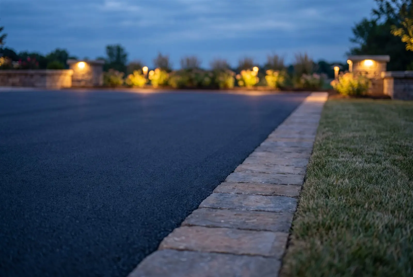 Nahdetail einer glatten neuen Asphalt-Einfahrt an einer sauberen Pflasterkante in der Dämmerung